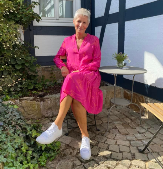 Eine blonde Frau im rosa Kleid mit weißen Sneakern auf einer Terrasse